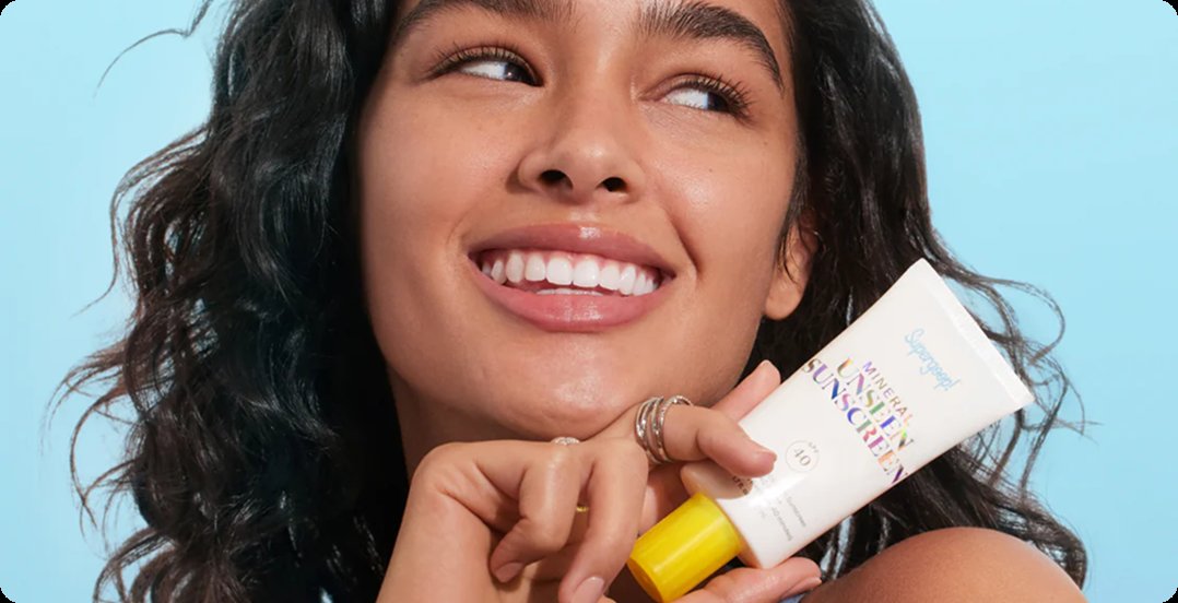 A woman holding a Supergoop sunscreen tube
