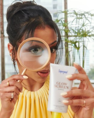 A shopper looking through a magnifying glass at a Supergoop tube