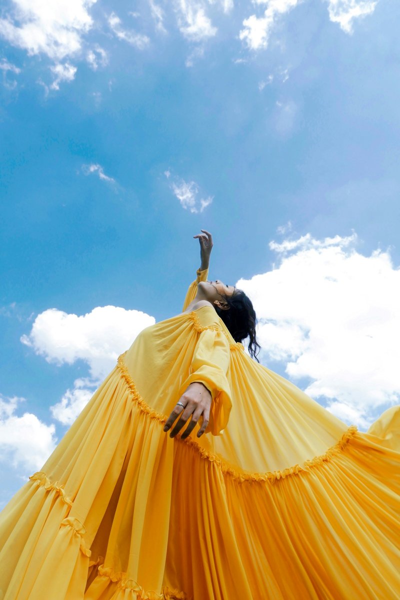 A woman in a yellow dress against a blue sky